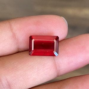 May include: A deep red gemstone with a rectangular emerald cut.