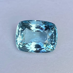 May include: A cushion-cut aquamarine gemstone with a light blue color. The gemstone is faceted and has a high degree of brilliance.
