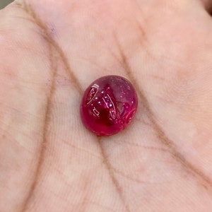 May include: A vibrant red gemstone cabochon, with a smooth, rounded surface and a slight shine.