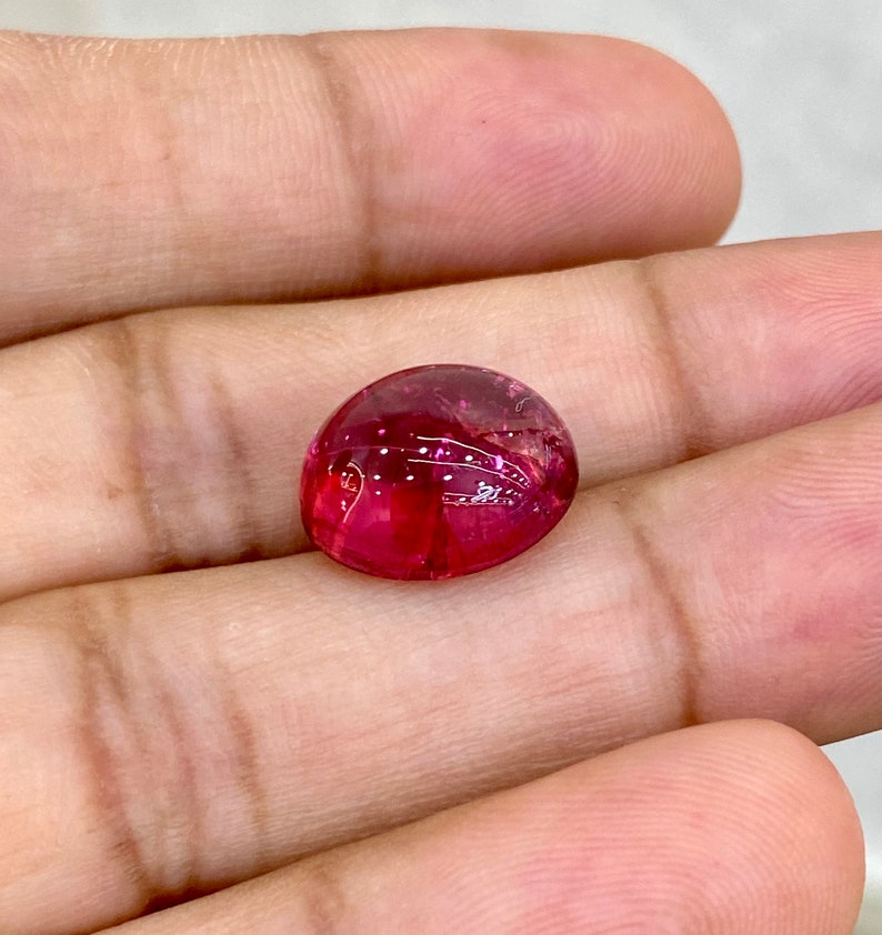 May include: A vibrant pink oval-shaped gemstone with a smooth, polished surface.