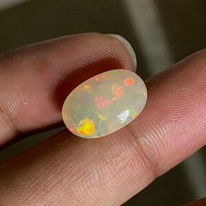 Pu&ograve; includere: Una pietra preziosa di opale ovale bianca con un arcobaleno di colori, tra cui giallo, arancione, rosso, verde e blu.