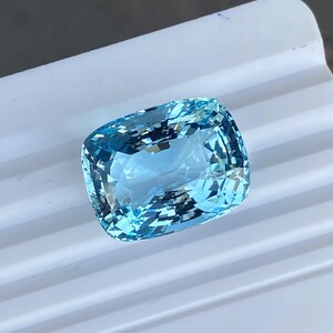 May include: A cushion-shaped aquamarine gemstone with a light blue color. The gemstone is faceted and has a high degree of brilliance.