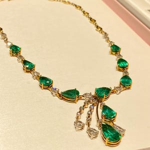 May include: A gold necklace featuring pear-shaped emeralds and small diamonds. The necklace has a delicate chain and a cluster of emeralds and diamonds that hang down. The emeralds are a vibrant green color.