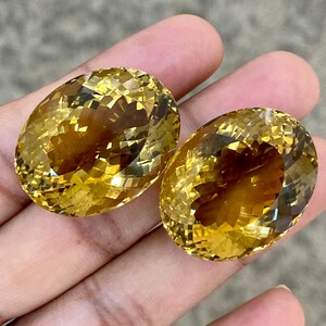 May include: Two oval-shaped, faceted, yellow citrine gemstones. The gemstones are a light to medium yellow color and have a high degree of clarity.
