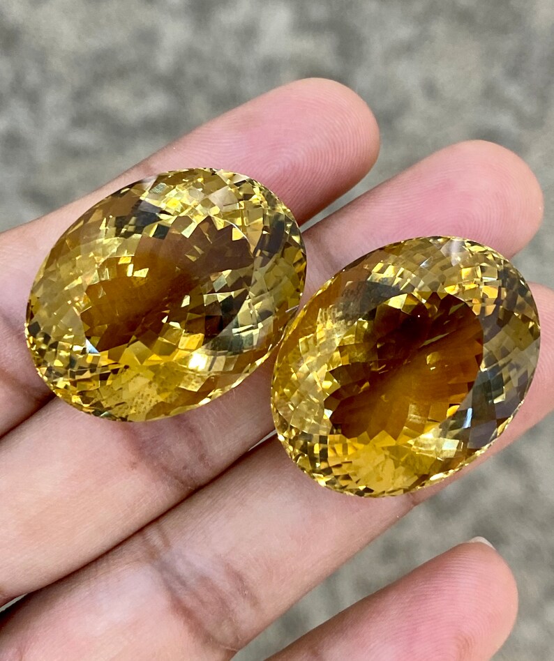 May include: Two oval-shaped, faceted, yellow citrine gemstones. The gemstones are a light to medium yellow color and have a high degree of clarity.
