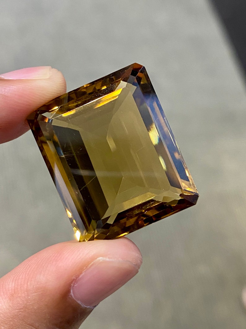 May include: A large, rectangular, faceted gemstone with a golden brown color.