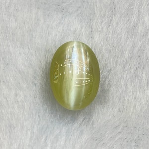 May include: A round, light green gemstone with a white, swirling pattern inside. The gemstone has a smooth, polished surface.