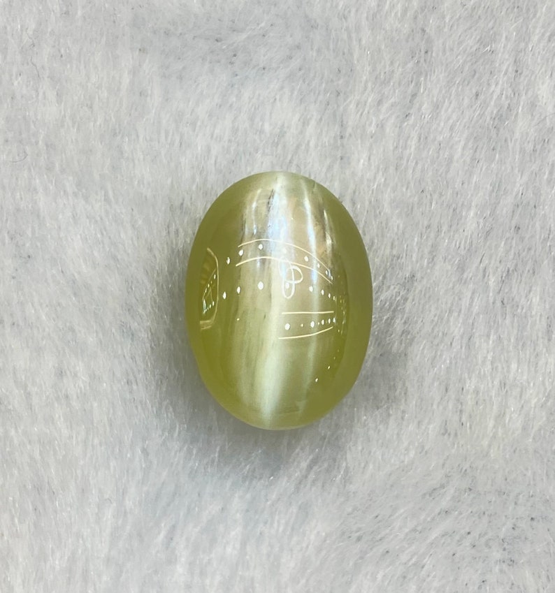 May include: A round, light green gemstone with a white, swirling pattern inside. The gemstone has a smooth, polished surface.