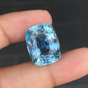May include: A large, cushion-cut aquamarine gemstone with a light blue color. The gemstone is faceted and has a high degree of brilliance.