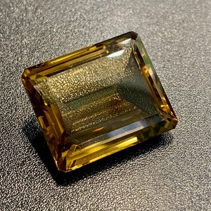 May include: A large, rectangular, faceted gemstone with a golden brown color. The gemstone is cut into a step cut style.