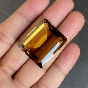 May include: A large, rectangular, faceted gemstone with a golden brown color. The gemstone is cut in an emerald shape.