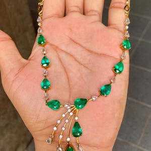 May include: A gold necklace featuring pear-shaped emeralds and small diamonds. The emeralds are a vibrant green, and the diamonds are clear. The necklace has a delicate design with a central cascade of emeralds and diamonds.