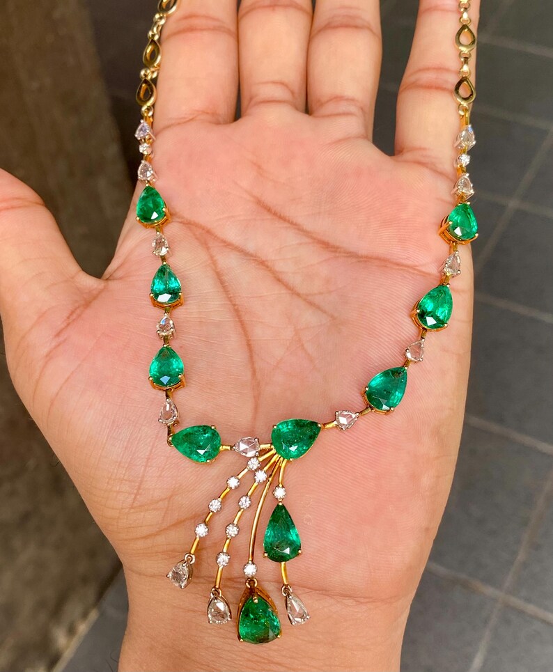 May include: A gold necklace featuring pear-shaped emeralds and small diamonds. The emeralds are a vibrant green, and the diamonds are clear. The necklace has a delicate design with a central cascade of emeralds and diamonds.