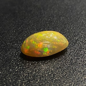 May include: A light green oval opal gemstone with flashes of red and green.
