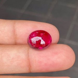 May include: A round, cabochon-cut, red gemstone with a high polish. The gemstone is set in a bezel setting and has a slight sparkle.
