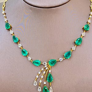 May include: A gold necklace featuring pear-shaped emeralds and diamond accents. The emeralds are a vibrant green, and the diamonds are clear. The necklace has a delicate design with a central cluster of emeralds and diamonds.