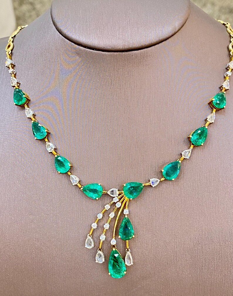 May include: A gold necklace featuring pear-shaped emeralds and diamond accents. The emeralds are a vibrant green, and the diamonds are clear. The necklace has a delicate design with a central cluster of emeralds and diamonds.