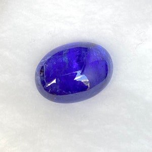 May include: A deep blue oval-shaped gemstone with a smooth, polished surface. The gemstone has a slight shimmer and is set against a white background.