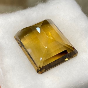 May include: A large, rectangular, faceted gemstone with a golden brown color. The gemstone is cut in a step-cut style and has a high polish.