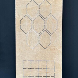May include: A wooden die-cut template with geometric shapes. The template features cut-out hexagons, a smaller floral design, and a grid pattern. The text "EP-HC-ST-1" is printed at the top. The wood has a light brown color.