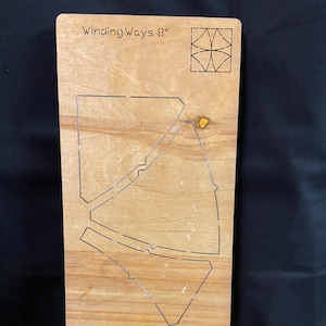 May include: A wooden quilting template with the text "Winding Ways 8"" and a geometric design. The template features cut-out shapes for quilting, with a light brown wood grain finish.