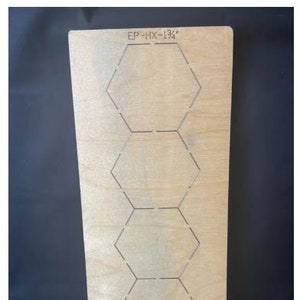 Puede incluir: Una tabla de corte de madera marrón claro con una serie de formas hexagonales. La tabla tiene líneas grabadas que definen las formas. El texto en la parte superior dice "EP-HX-1 3/4". Las formas hexagonales miden 4,4 cm.