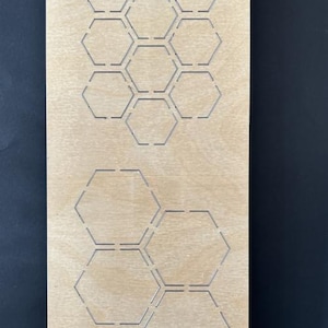 May include: A wooden die-cut featuring a honeycomb design. The rectangular die-cut has multiple hexagonal cutouts. The text "EP-HX-ST-¾-1¼" is printed at the top. The die-cut is made of light brown wood.