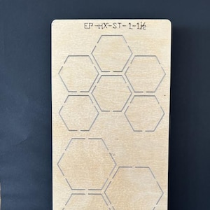 May include: A wooden die with nine hexagonal cutouts. The die has the text "EP-HX-ST-1-1½" printed at the top. The die is light brown and sits against a dark blue background.