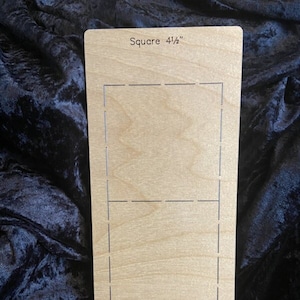May include: A wooden square cutting template with a 4 1/2 inch square marked out on it.