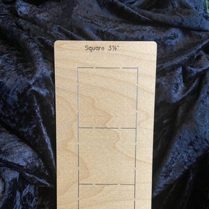 Puede incluir: Plantilla rectangular de madera con cortes cuadrados. El texto "Square 3 1/2" está grabado en la parte superior. La plantilla es de madera clara.