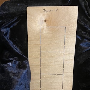 May include: A light-coloured wooden square with a rectangular cutout design. The text "Square 3" is printed at the top. The design features four rectangular cutouts. The wood has a natural grain.