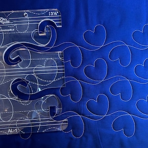 Könnte beinhalten: Eine transparente Kunststoff-Quiltvorlage mit dem Text "I love to quilt..." und "www.ilovetoquilt.nl" darauf gedruckt. Die Vorlage zeigt ein Design aus geschwungenen Linien und Herzen. Die Vorlage ist mit "AL-1" gekennzeichnet und misst 13 1/2 Zoll.