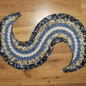 Könnte beinhalten: Ein blauer und beiger Teppich mit floralem Muster in Form einer großen S-Kurve. Der Teppich ist aus Stoff und hat einen gekräuselten Rand.