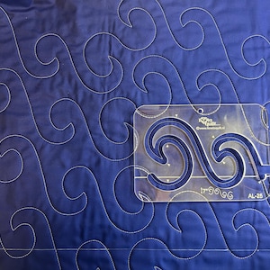 Puede incluir: Primer plano de una tela acolchada azul con un patrón de ondas cosido con hilo blanco. Una plantilla de acolchado acrílica transparente con un diseño de ondas a juego se coloca sobre la tela. La plantilla tiene el texto "I love to quilt..." y "AL-25".