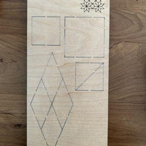 Puede incluir: Una tabla de corte de madera de color marrón claro con formas geométricas y el texto "Scarlet EP-8P-SC-2'". Presenta patrones cuadrados, de diamante y de estrella, ideal para proyectos de manualidades. La tabla es adecuada para varios proyectos creativos.