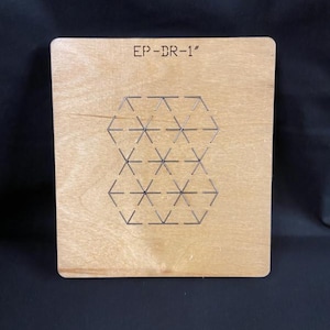 May include: A square wooden die with the text "EP-DR-1" engraved at the top. The die features a geometric pattern of interconnected shapes made of thin metal rods. The wood has a light brown color.