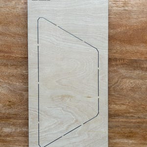 May include: A light-colored wooden die-cut with a geometric design and the text "1/2-HX-4 1/2". The die-cut features a series of dotted lines outlining a shape, and a geometric symbol in the upper left corner.