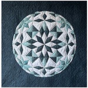 Pode incluir: Um tecido acolchoado azul-turquesa com um padrão geométrico branco e azul-turquesa no centro. O padrão é um círculo com um design de estrela.