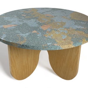 Puede incluir: Una mesa de centro redonda con una tapa única de mármol en tonos azules, dorados y rosados. La mesa tiene cuatro patas de madera con un diseño curvo.