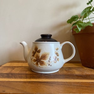 Könnte beinhalten: Eine braune und weiße Teekanne mit braunem Deckel und floralem Muster. Die Teekanne steht auf einer Holzoberfläche.