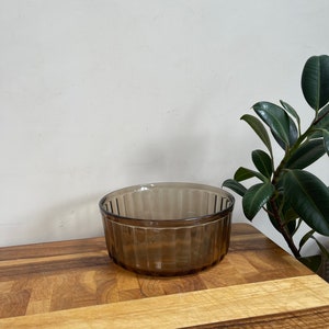 May include: A brown glass ramekin with a fluted design. The ramekin is sitting on a wooden cutting board.
