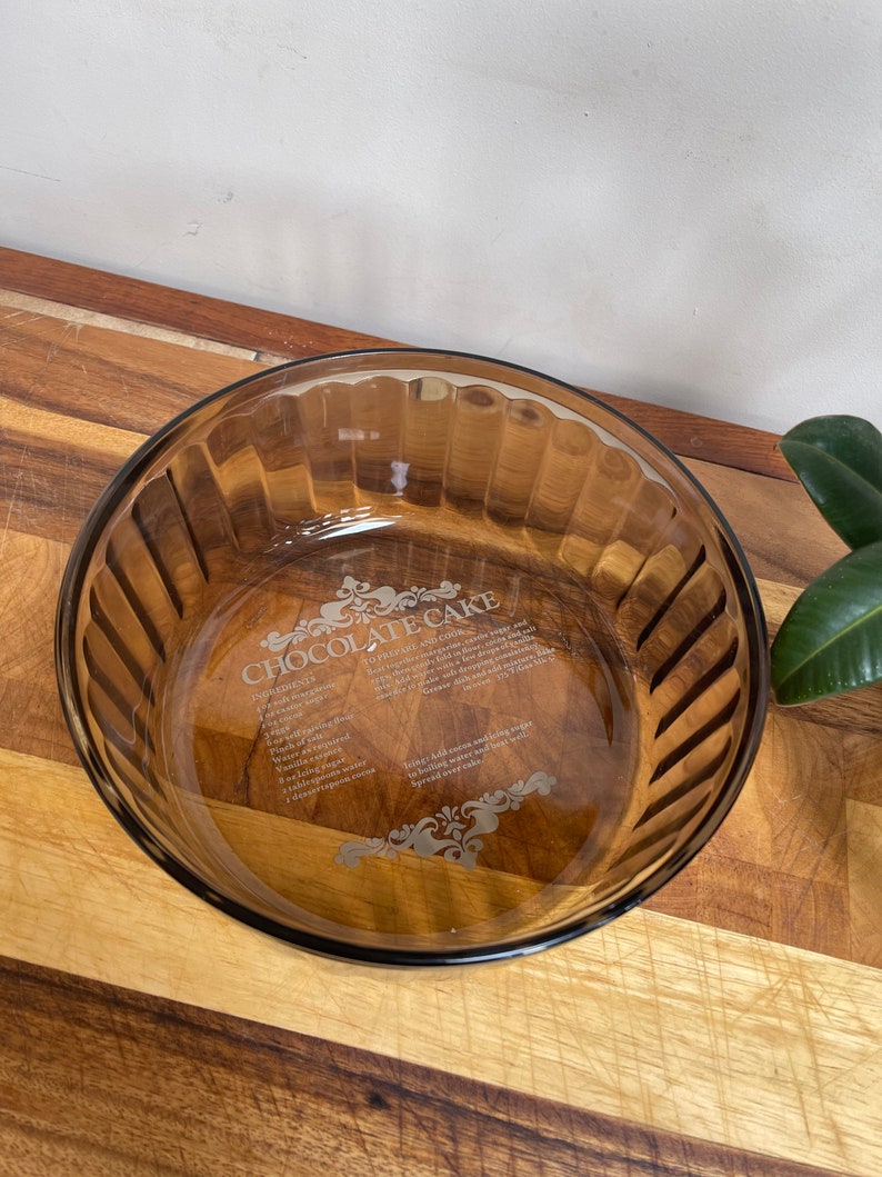 May include: A brown glass baking dish with a recipe for chocolate cake etched into the bottom. The recipe includes ingredients such as flour, sugar, eggs, and cocoa powder.