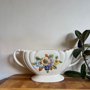 May include: White ceramic planter with two handles and a floral design. The flowers are in shades of blue, yellow, orange, and green.