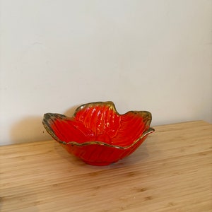 Könnte beinhalten: Orangefarbene Keramik Schale in Blumenform mit goldenen Akzenten. Die Schale steht auf einer Holzoberfläche.