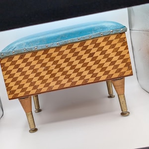 Puede incluir: Un reposapiés tapizado en azul con un patrón de madera a cuadros en los lados y tres patas de madera con pies de latón.