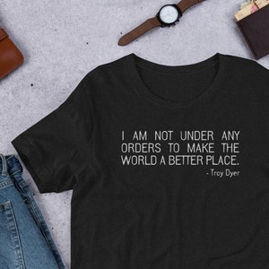 May include: A black t-shirt with a white quote that reads "I am not under any orders to make the world a better place. - Troy Dyer"