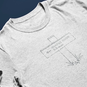 May include: Gray t-shirt with a black and white graphic of a sign that reads "Morafee Khor 0.5 miles".