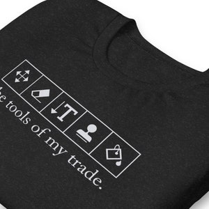 May include: Black t-shirt with white text that reads "These tools of my trade."  The text is surrounded by five white icons: a resize icon, an eraser, a text icon, a person icon, and a shopping bag icon.