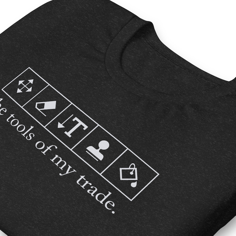 May include: Black t-shirt with white text that reads "These tools of my trade."  The text is surrounded by five white icons: a resize icon, an eraser, a text icon, a person icon, and a shopping bag icon.