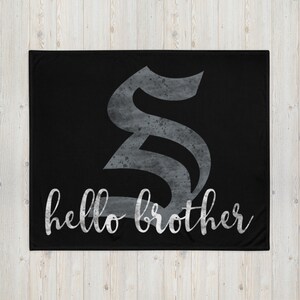 May include: Black fleece blanket with a large, silver, stylized letter "S" and the text "hello brother" in a white, cursive font.